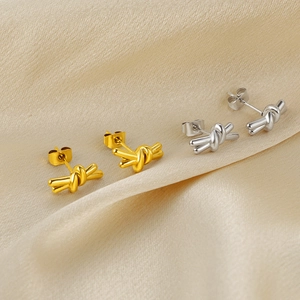 Polished gold and silver knot stud earrings displayed on elegant silk fabric background