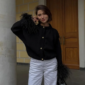 Detailaufnahme der schwarzen Strickjacke mit Federbündchen und goldenen Metallknöpfen