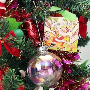 Iridescent clear Christmas ball ornament hanging on a festive green pine tree branch