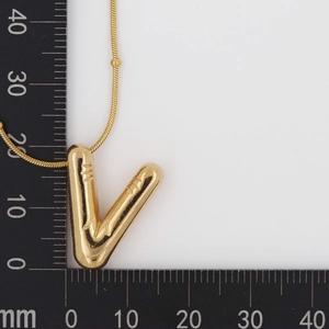 Macro shot of gold V-shaped letter pendant on ruler showing 20mm height dimension