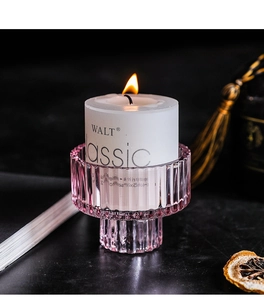 Detail of pink ribbed glass candle holder with a lit white pillar candle and warm glow
