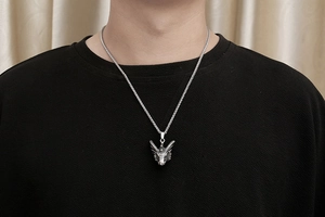 Détail du pendentif dragon en argent avec cornes sur une chaîne tressée portée par un homme