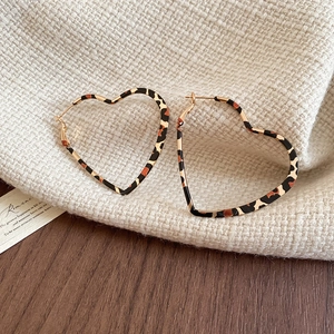Detail shot of heart-shaped leopard print earrings on soft beige knit fabric
