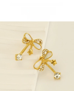 Detail of gold stainless steel bow earrings with zircon and shell inlay on wavy stand