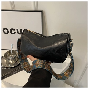 Detail of soft black leather bag featuring a wide blue and gold peacock pattern strap