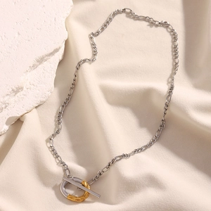 Vue détaillée du collier à fermoir OT bicolore avec chaîne Figaro sur tissu beige