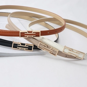 Detail of four thin leather belts in khaki, brown, black, and beige with gold buckles