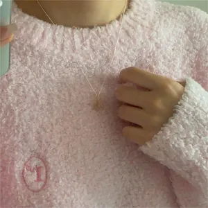 Close-up of a minimalist gold heart pendant necklace worn on a pink fuzzy sweater