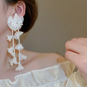 Close-up of white chiffon flower earrings with long beaded tassels on model's ear