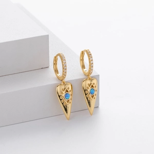 Detail of gold evil eye drop earrings with blue crystal on white geometric blocks