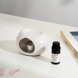 Ceramic essential oil burner with lemon oil and metal candle on white surface