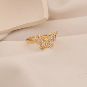 Eleganter goldener Schmetterlingsring mit weißen Zirkonia-Steinen auf beigem Stoff
