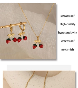 Détail d'un ensemble de bijoux fraise dorés avec émail rouge et feuilles vertes sur tissu