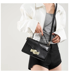 Detail of black faux leather crossbody bag with crocodile texture and gold wave buckle
