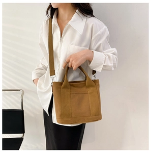 Brown canvas tote bag detail showing hand strap and adjustable shoulder strap worn by model