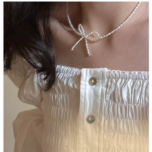 Detail showing elegant pearl bow necklace on white pleated shirt with soft lighting