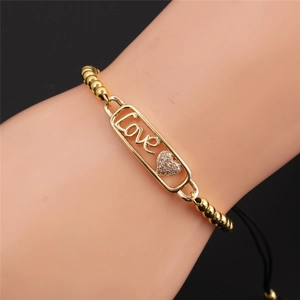 Dettaglio del bracciale placcato oro con ciondoli Love e zirconi su polso femminile