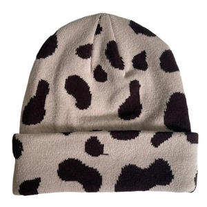 Detail of the knit texture and black cow print on this beige winter beanie hat