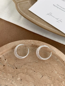 Macro detail of silver C-shaped earrings with layered texture on a stone display