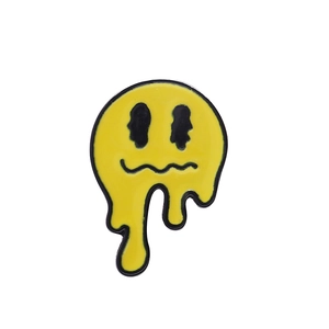 Détail d'un pin's émaillé jaune en forme de smiley fondant avec contours noirs