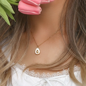 Close-up of gold avocado pendant necklace worn by model with pink tulip flowers