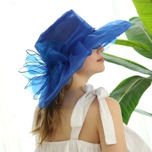 Detail of royal blue mesh sun hat with a large decorative flower worn by a model outdoors