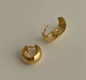 Close-up of chunky gold geometric hoop earrings with polished metal finish on beige