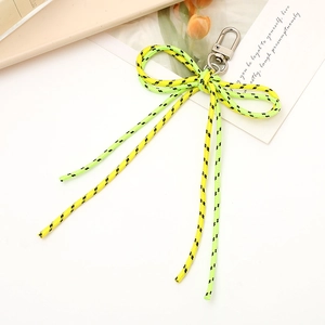 Detail of yellow and green woven bow keychain with a metal swivel clasp on a white desk