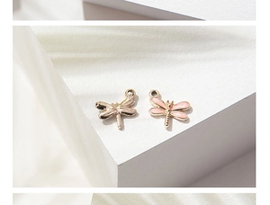 Macro shot of gold and pink enamel dragonfly charms on a minimalist white background