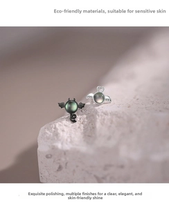Detailed view of silver angel and black devil studs with iridescent pearls on a stone