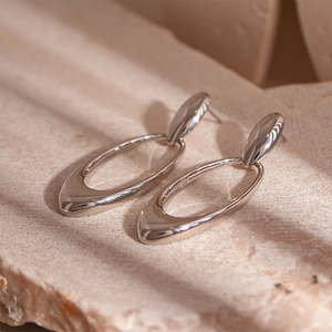 Macro shot of silver geometric oval earrings resting on a textured stone surface