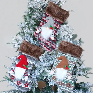 Three plush gnome Christmas stockings with knitted patterns hanging on a snowy tree