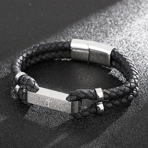 Vue macro du bracelet en cuir tressé et de la plaque métallique argentée gravée d'une croix