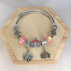 Detail of steel cable bracelet with pink beads, elephant and crown charms on wood