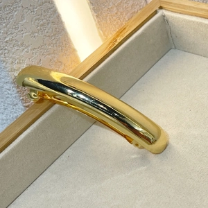 Close-up of polished gold-finished curved metal spring hair clip on a velvet tray
