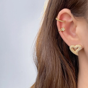 Close-up of sparkling heart and star zircon earrings worn by a model in gold finish