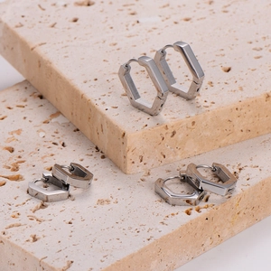Polished silver pentagonal hoop earrings displayed on natural stone platforms