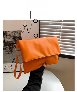 Detalle del bolso de sobre naranja con cremallera dorada y correa para la muñeca