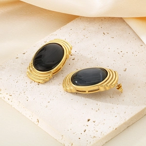 Detailed view of vintage gold stainless steel earrings with oval black stones on stone surface