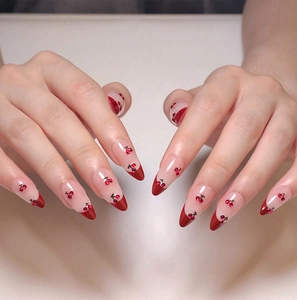 Detail of almond-shaped press-on nails with red French tips and cherry 3D art design