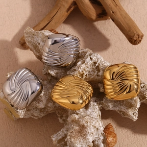 Macro view of gold and silver square wing earrings with water ripple texture on coral