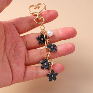 Detail of heart clasp gold keychain with black enamel flowers and a white pearl