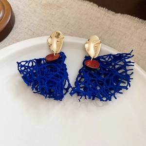 Detail shot of vintage fan-shaped earrings with blue woven fabric on a ceramic dish