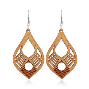 Close-up of brown wooden teardrop earrings with geometric hollow carvings and metal hooks