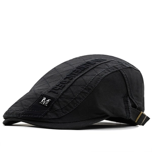 Detail view of black quilted cotton newsboy hat with silver M metal badge and embroidery