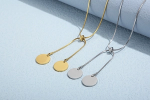 Detail of gold and silver snake chain necklaces with round pendants on blue surface