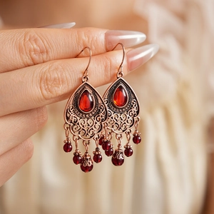 Dettaglio macro di orecchini vintage in bronzo con gemme rosse e eleganti nappe