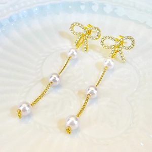 Detail view of gold bow earrings with shimmering rhinestones and long pearl tassels