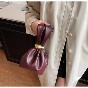 Detail of burgundy PU leather handbag with elegant gold metal ring handle and pleats