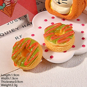 Macro detail of miniature resin donut charms with green icing and red stripes on a plate